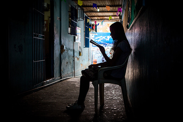 Uma jovem lendo sentada em uma cadeira, em um corredor escuro